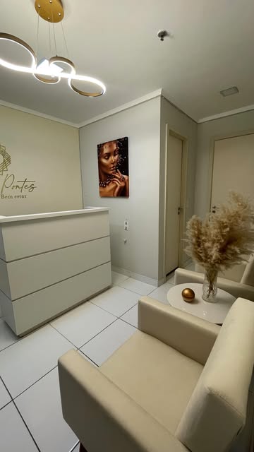 Recepção do espaço: balcão branco, poltrona bege e quadro na parede.